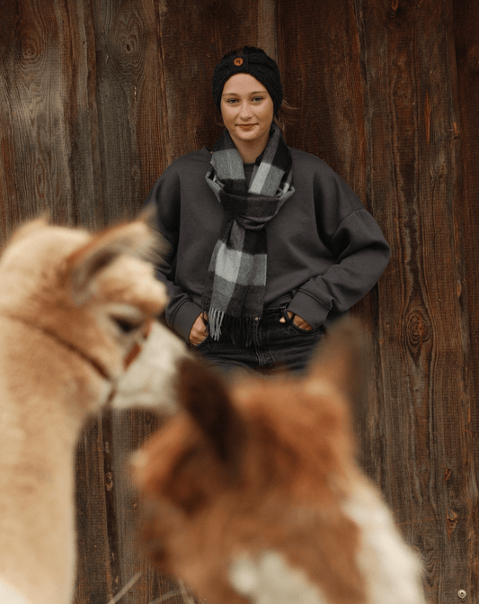 Vorteile von Alpakawolle: Junge Frau mit Alpakas vor Holzwand, die Gemütlichkeit und Stil demonstriert.