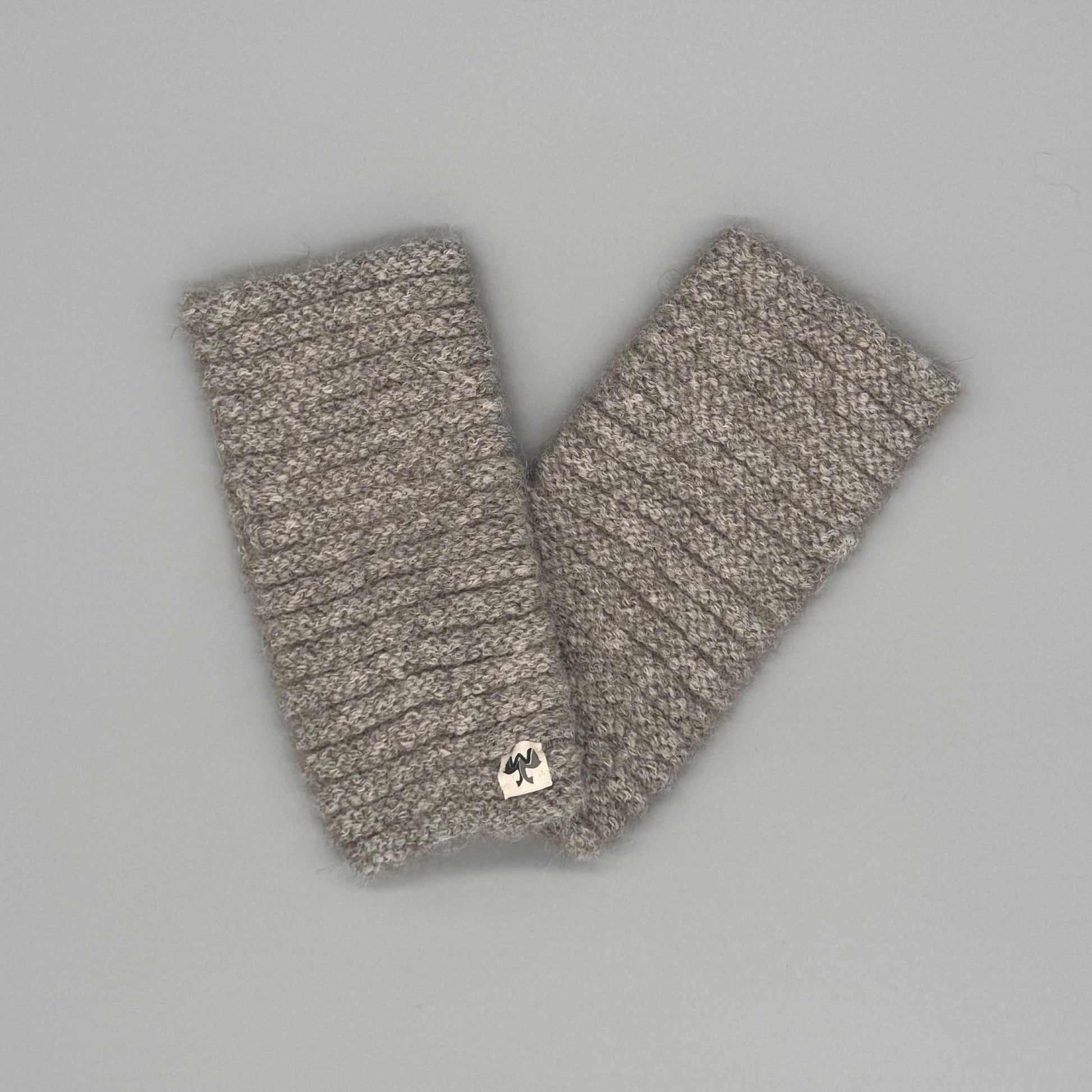 Beige Alpaka Pulswärmer aus Baby-Alpakawolle im Röllchenmuster auf grauem Hintergrund.