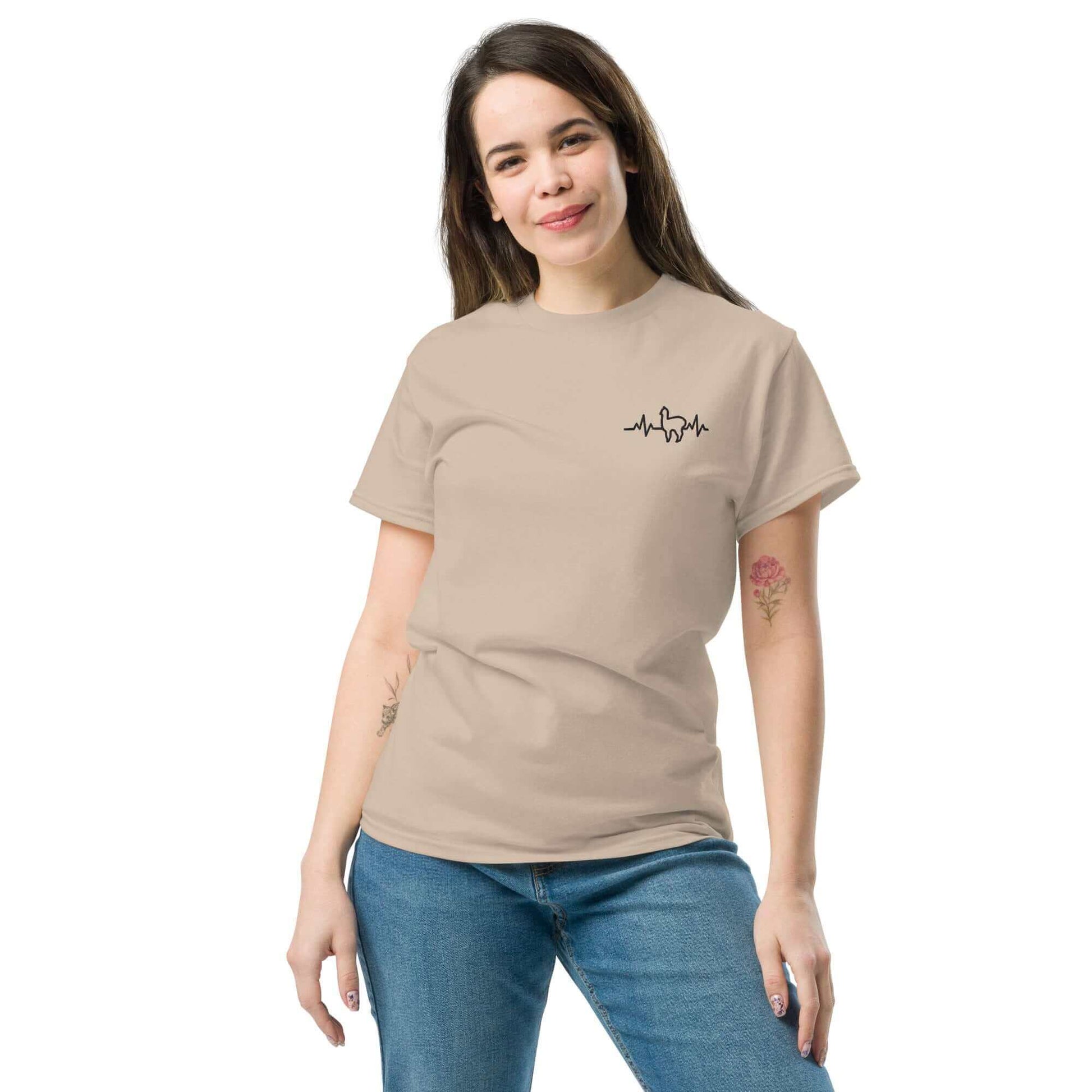 Frau trägt ein beiges Unisex Alpaka Herzschlag T-Shirt mit niedlichem Alpaka-Motiv – ideal für Alpaka-Enthusiasten und Fans von Alpaka Produkten.