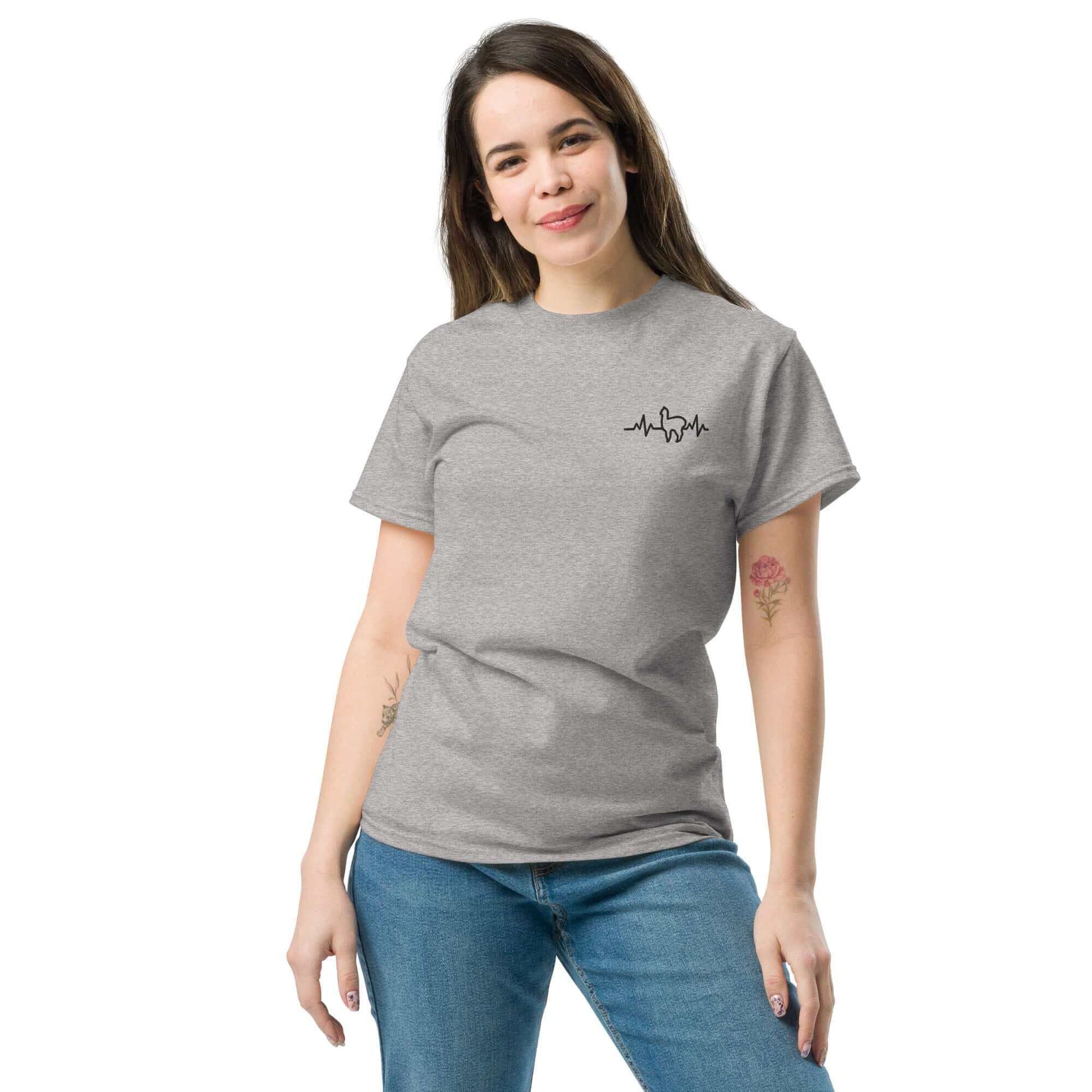 Frau trägt graues Unisex Alpaka Herzschlag T-Shirt, perfekt für Alpaka Enthusiasten.